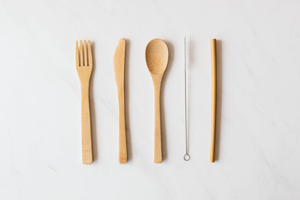 Top view of brush for cleaning tubes with tube placed in row with wooden cutlery on white marble surface