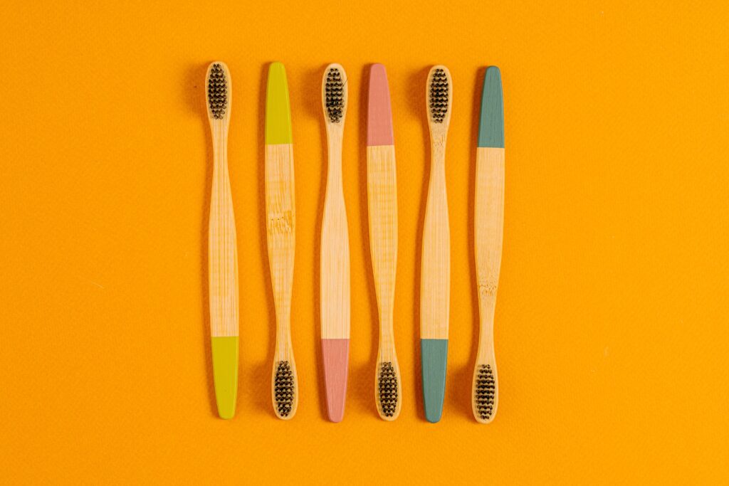 Six bamboo toothbrushes with colorful tips on a vibrant orange surface.