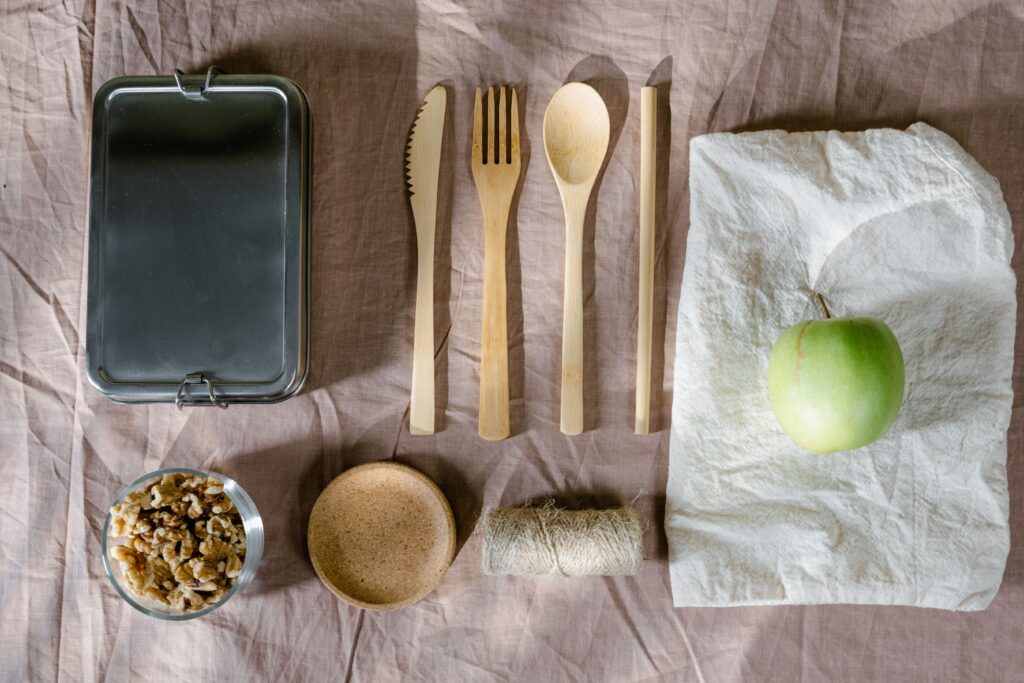 A flat lay of eco-friendly lunch items including wooden cutlery and a green apple.